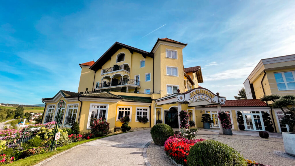 Wellnessurlaub im Hotel Jagdhof im bayerischen Wald in Röhrnbach. Die Vorfahrt des großen luxus-Hotels angestrichen in gelb, mit rotem Ziegeldach bei strahlendem schönen Wetter und Wolkenlosem Himmel.